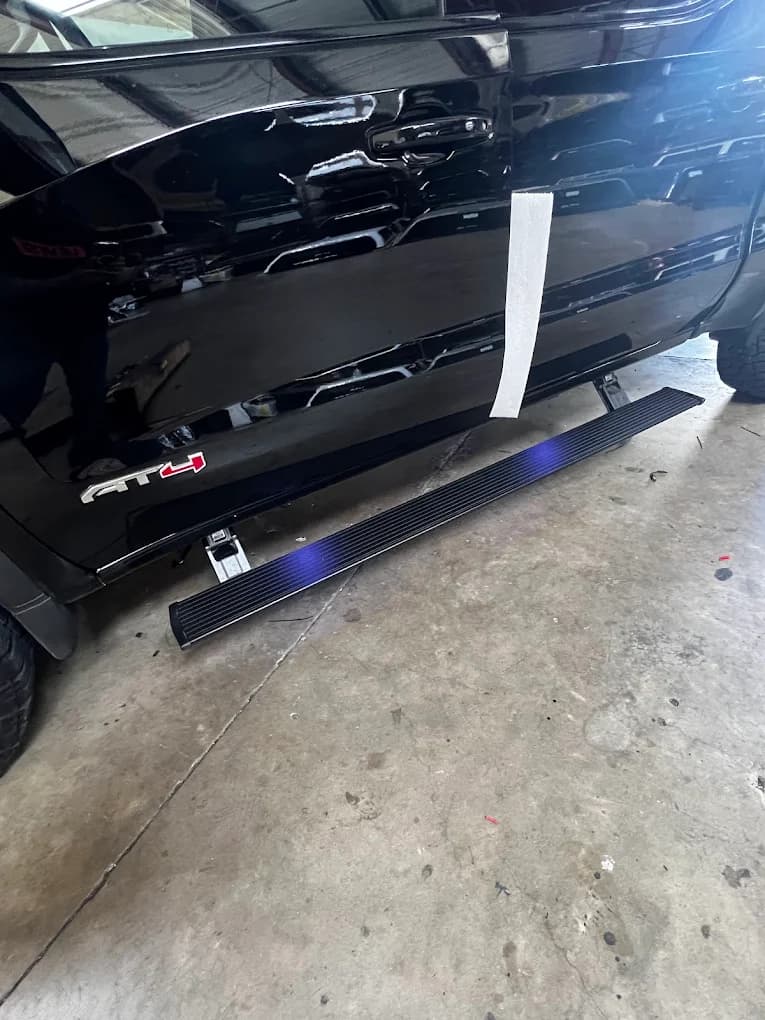 Powered retracting running board extended beneath a black pickup on a service-bay floor