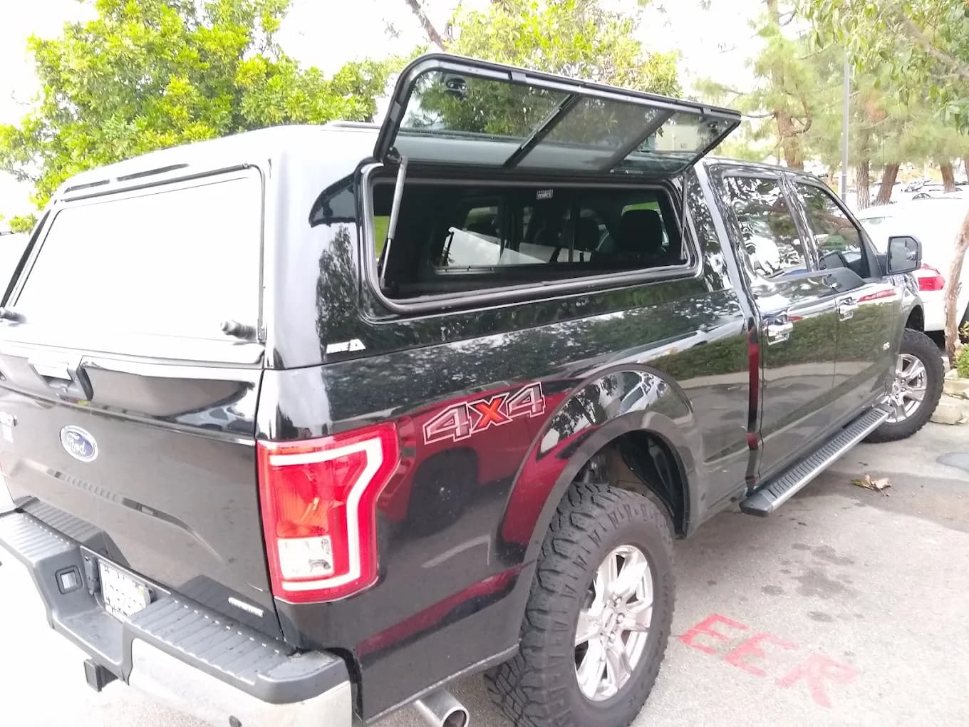 Black Ford F-150 4x4 with a color-matched cap, gullwing side door propped open