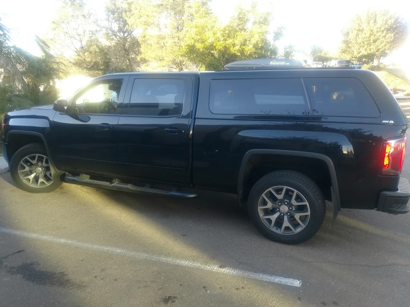 Black GMC Sierra with an A.R.E. cap carrying a roof-mounted cargo box, plus step bars