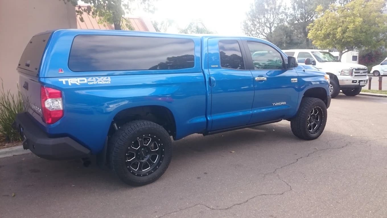 Blue Toyota Tundra TRD with a color-matched cap and step bars, parked beside the shop