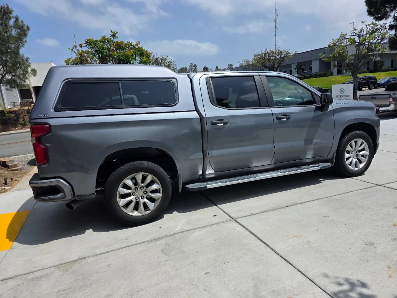 Grey Chevrolet Silverado with a color-matched A.R.E. cap and chrome step bars on the shop apron