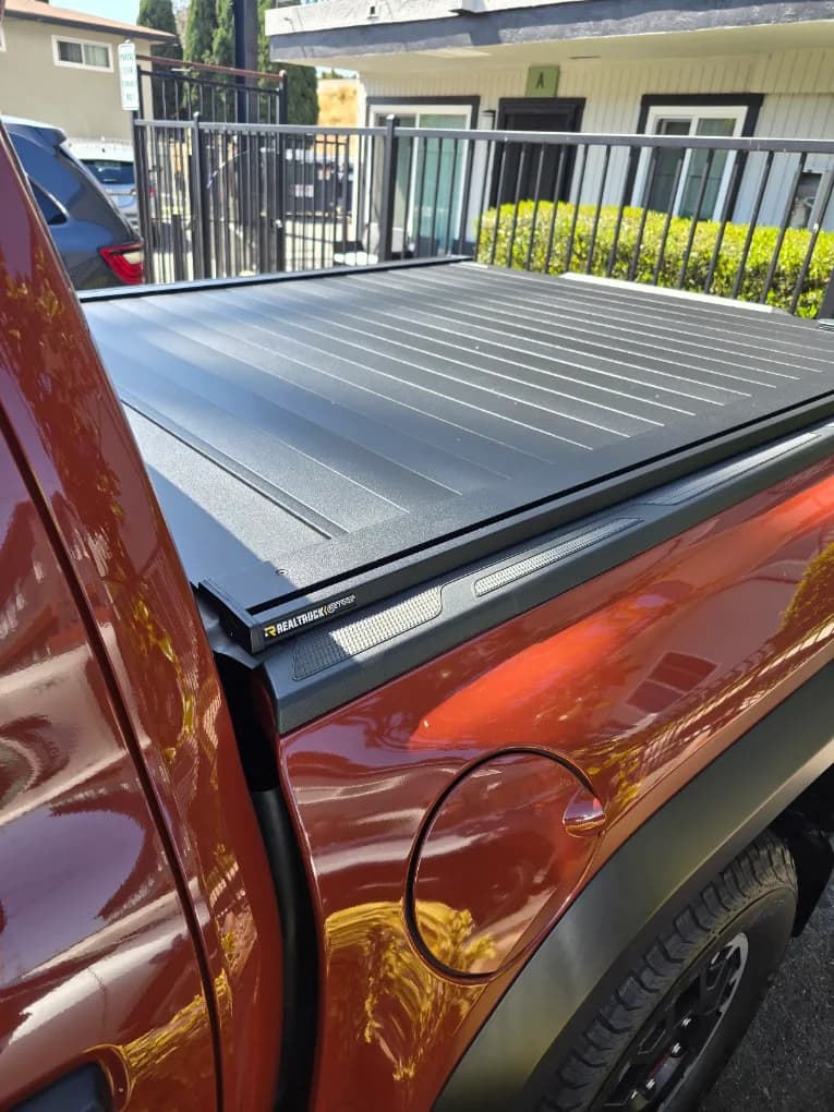 Close-up of a retractable hard tonneau cover on an orange Toyota Tacoma