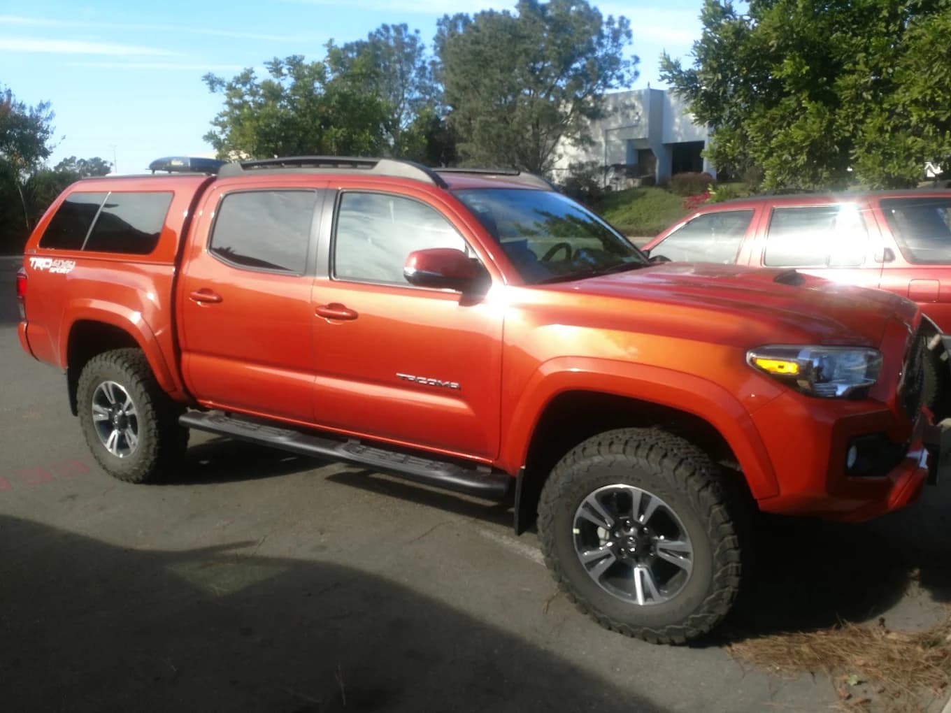 Orange Toyota Tacoma TRD with a color-matched camper shell and roof rails