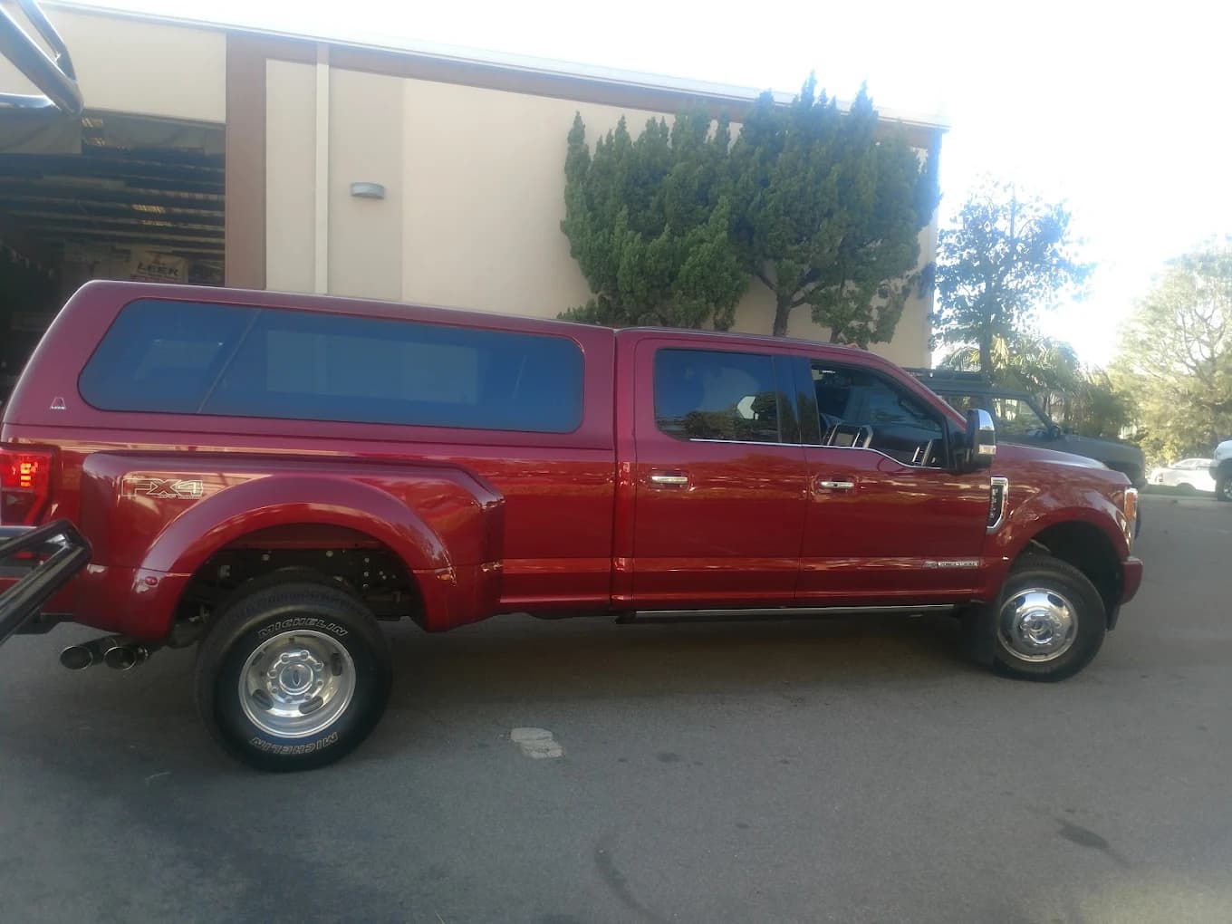 Red Ford F-350 dually with a long-bed color-matched LEER cap, parked beside the shop