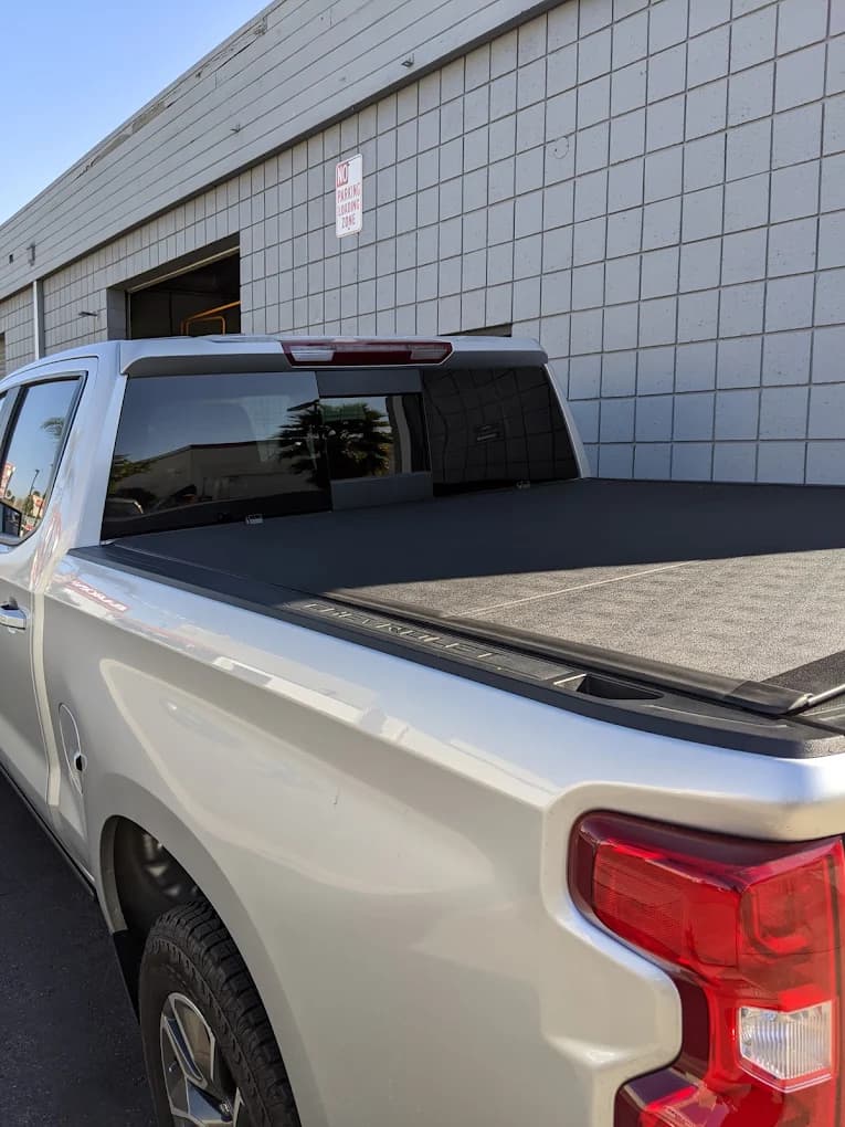 Soft roll-up tonneau cover fitted to a silver Chevrolet Silverado beside the shop building