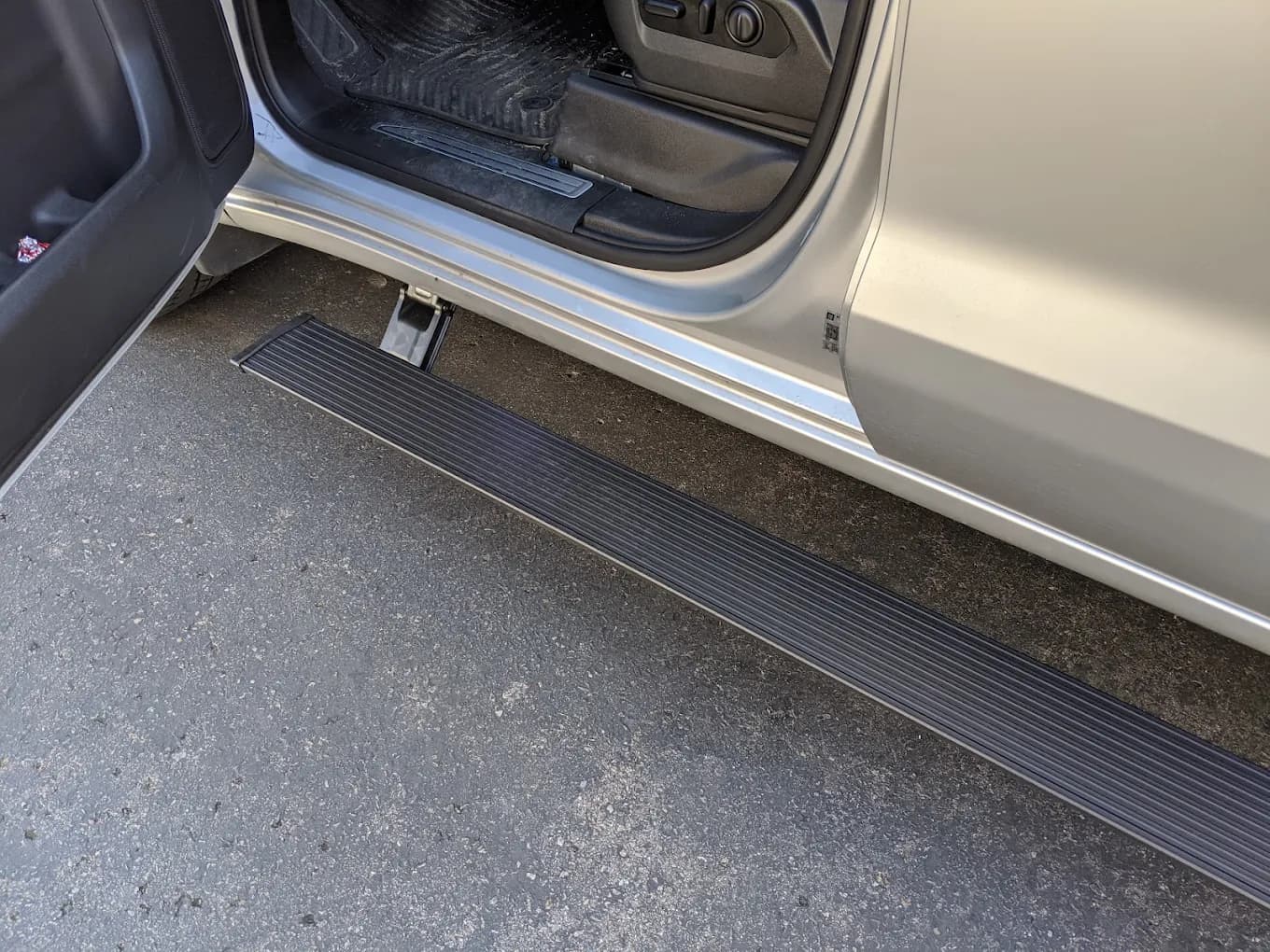 Powered retracting running board extended beneath the open door of a silver pickup