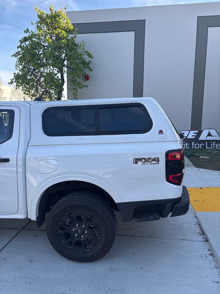 White Ford Ranger FX4 with a color-matched cap, parked beside the shop building