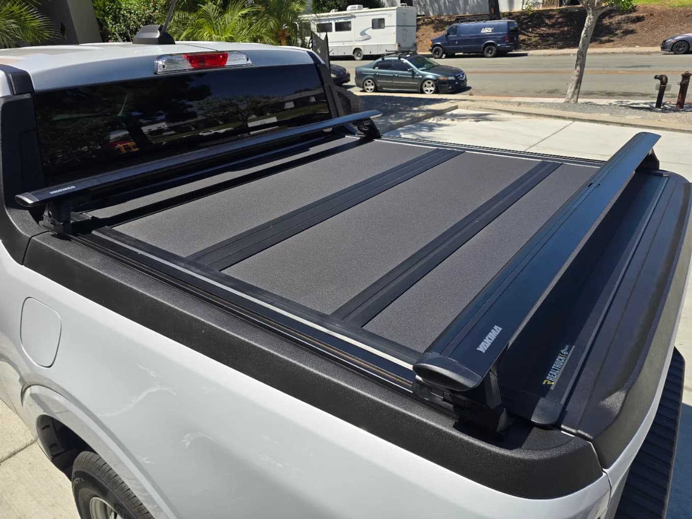 Folding hard tonneau cover on a white pickup with Yakima crossbars mounted over the bed